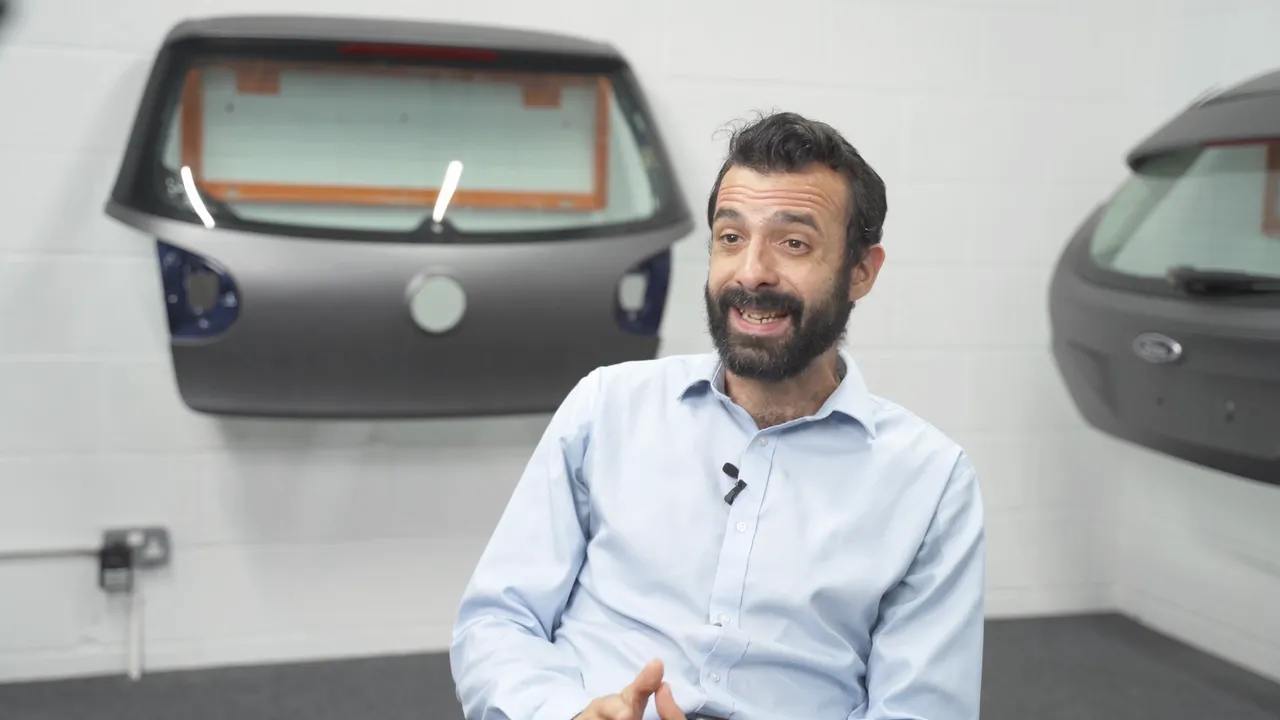A still from the Global Tint film: the speaker with tinted car tailgates on the wall behind him