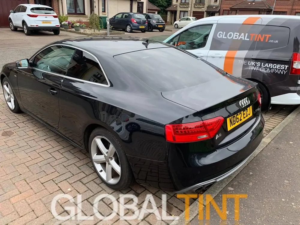 Black Audi A5 coupe with dark rear glass, parked beside a Global Tint van