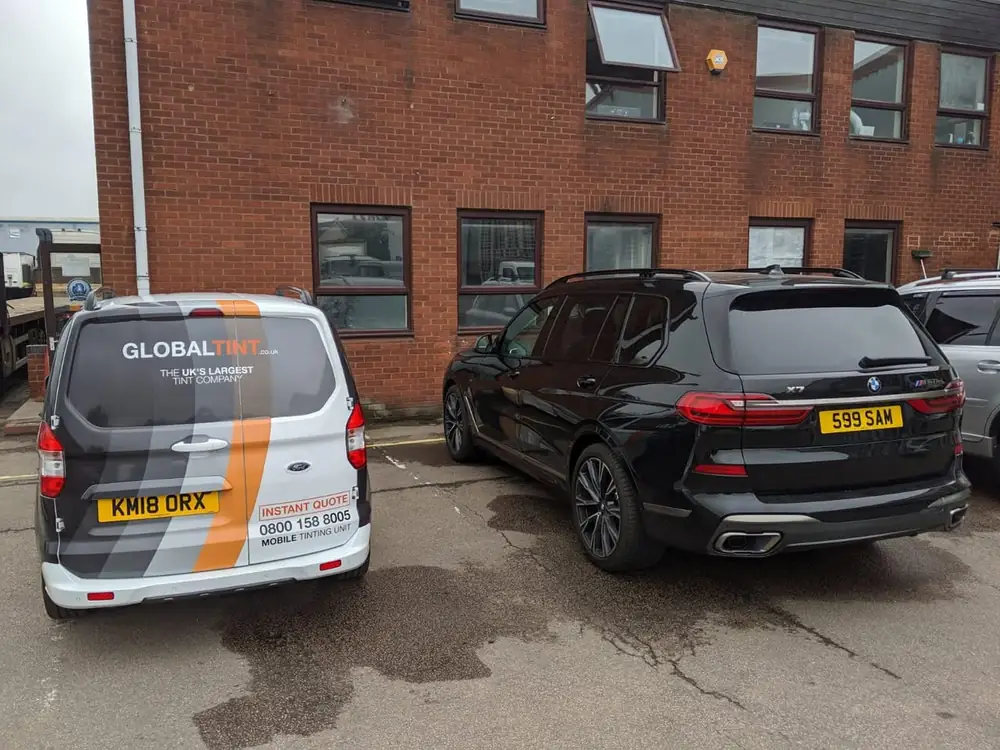 Black BMW X7 with dark rear side windows and rear windscreen, parked beside a Global Tint van.