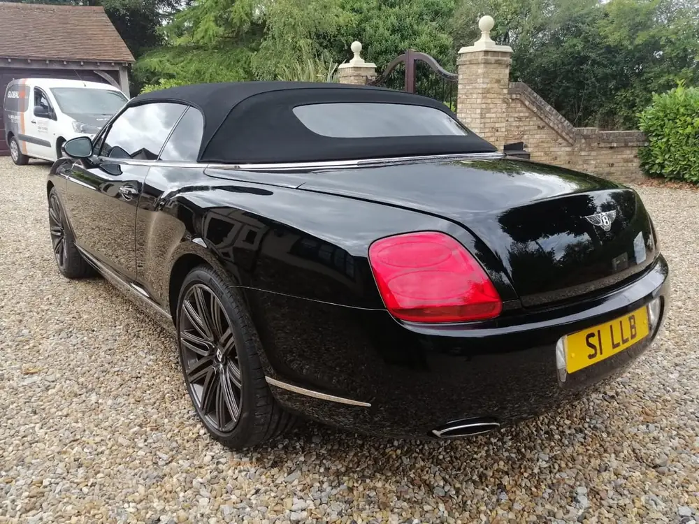 Black convertible with dark rear side glass and a black fabric roof, parked on gravel.
