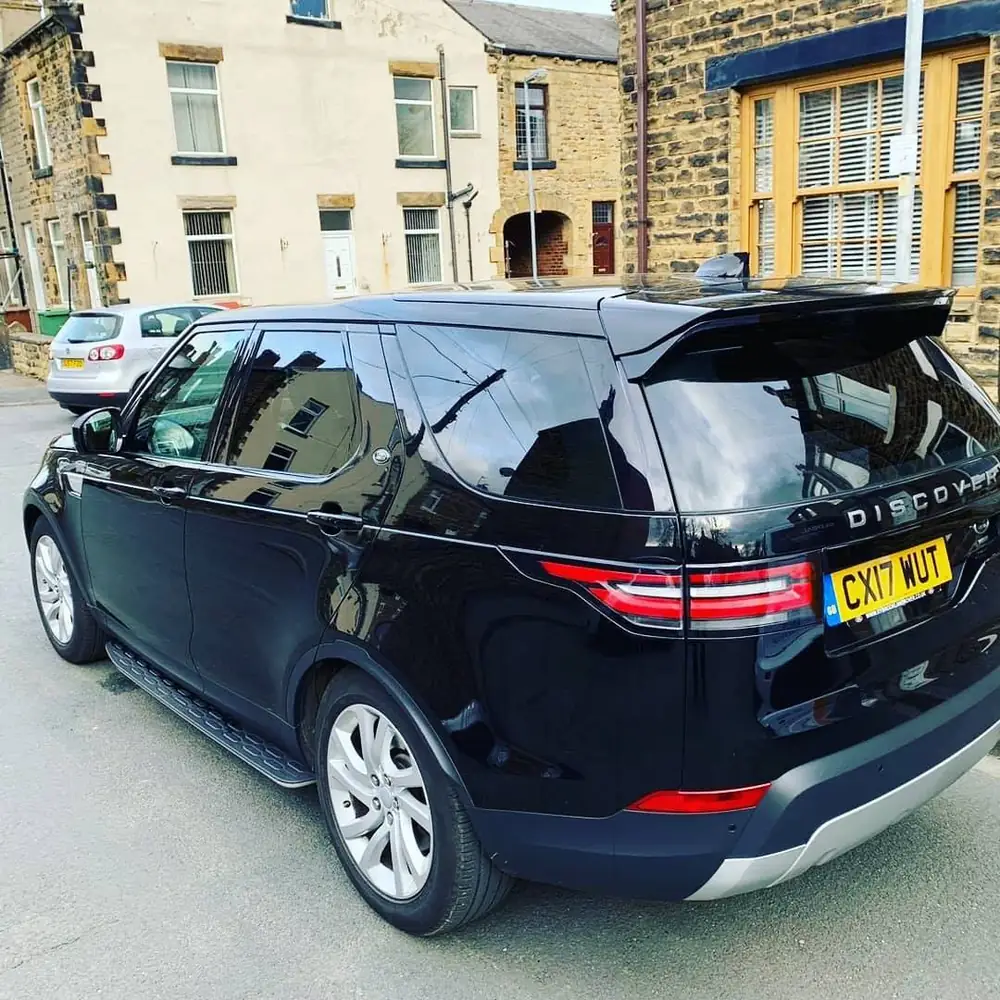 Black Land Rover Discovery with dark rear side windows and rear windscreen, viewed from the rear.