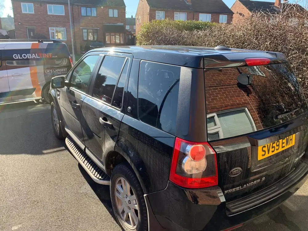 Black Land Rover Freelander 2 with dark rear side windows and rear windscreen, beside a Global Tint van.