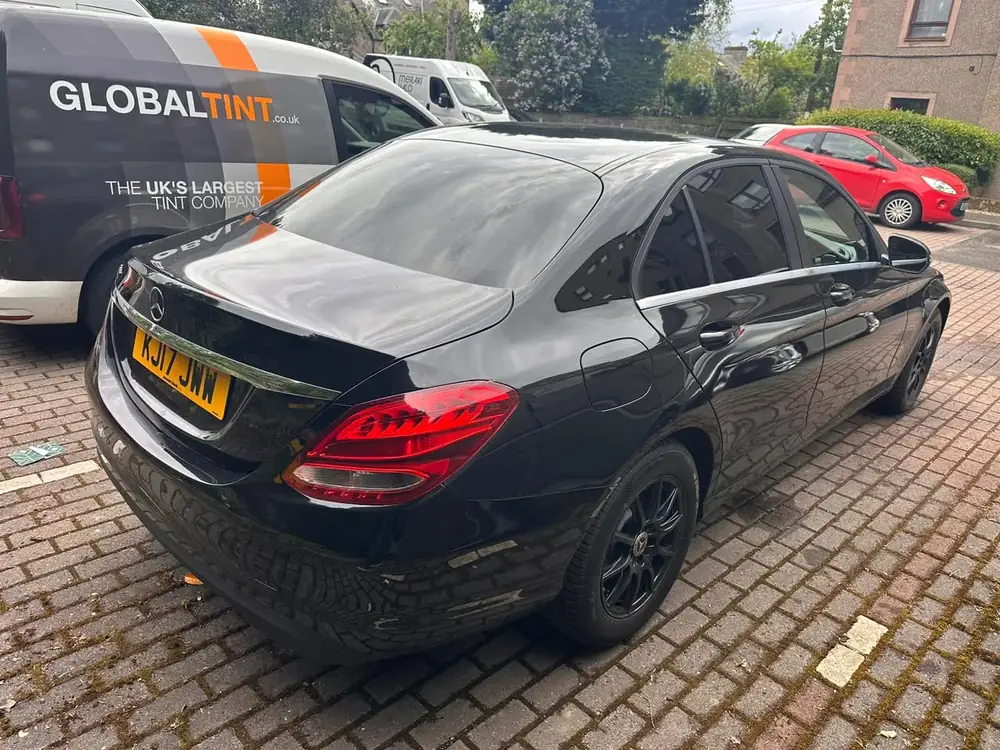 Black Mercedes-Benz C-Class with dark rear side windows and back windscreen, parked on block paving.