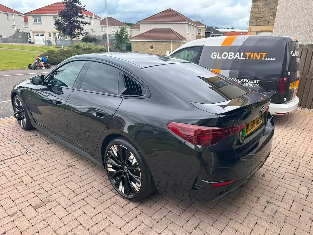 Black Mercedes-Benz CLA with dark rear side windows, parked beside a Global Tint van on a driveway