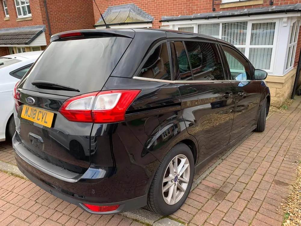 Black MPV with dark rear side windows, seen from behind on a brick driveway