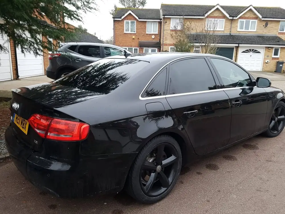 Black saloon with dark rear windows and black wheels, viewed from behind on a driveway