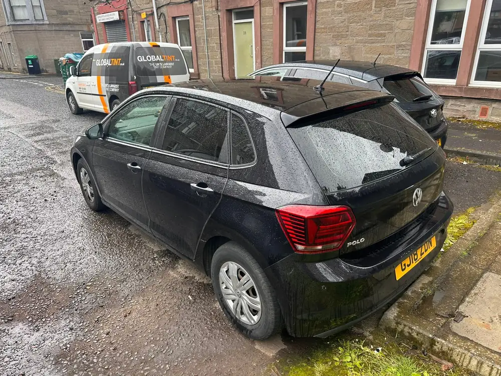 Wet black Volkswagen Polo with tinted rear side glass and back windscreen, parked beside another car