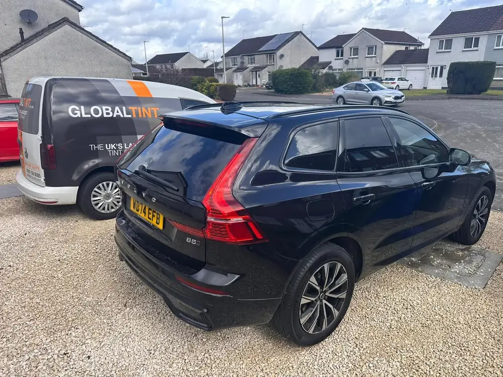 Black Volvo XC60 with dark rear side windows and rear windscreen, parked on gravel beside a Global Tint van