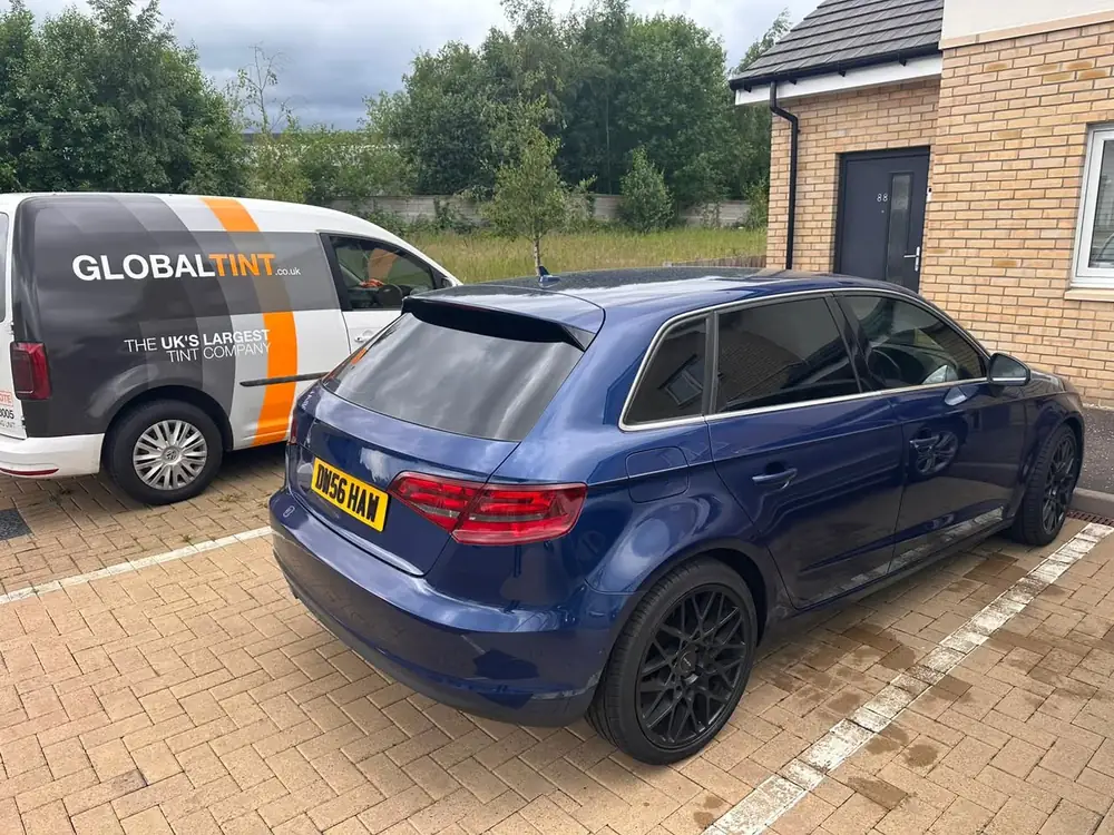 Blue Audi A3 Sportback with dark rear windows and back windscreen, parked on block paving beside a Global Tint van