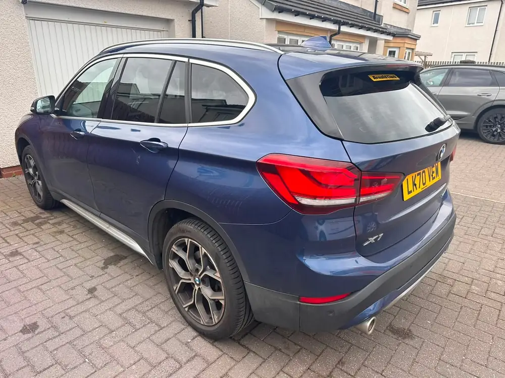Blue BMW X1 with tinted rear side windows and back windscreen, parked on a paved driveway