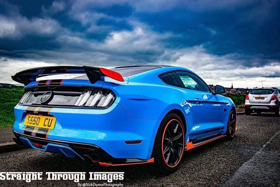 Blue coupe with a dark rear quarter window, black wheels and a large rear spoiler, parked outdoors