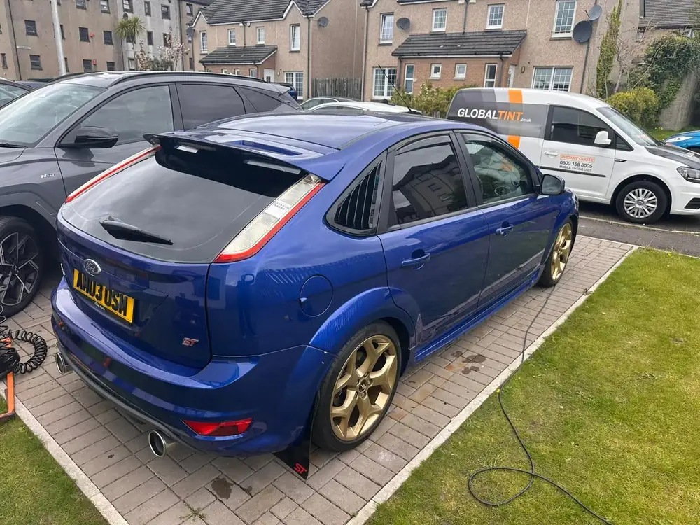 Blue Ford Focus ST on block paving with its visible rear side window and rear windscreen tinted dark