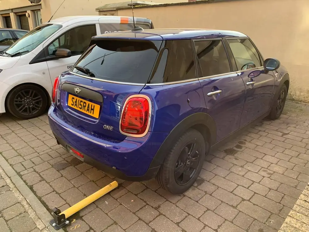Blue MINI One hatchback with a dark rear windscreen, parked beside a white van