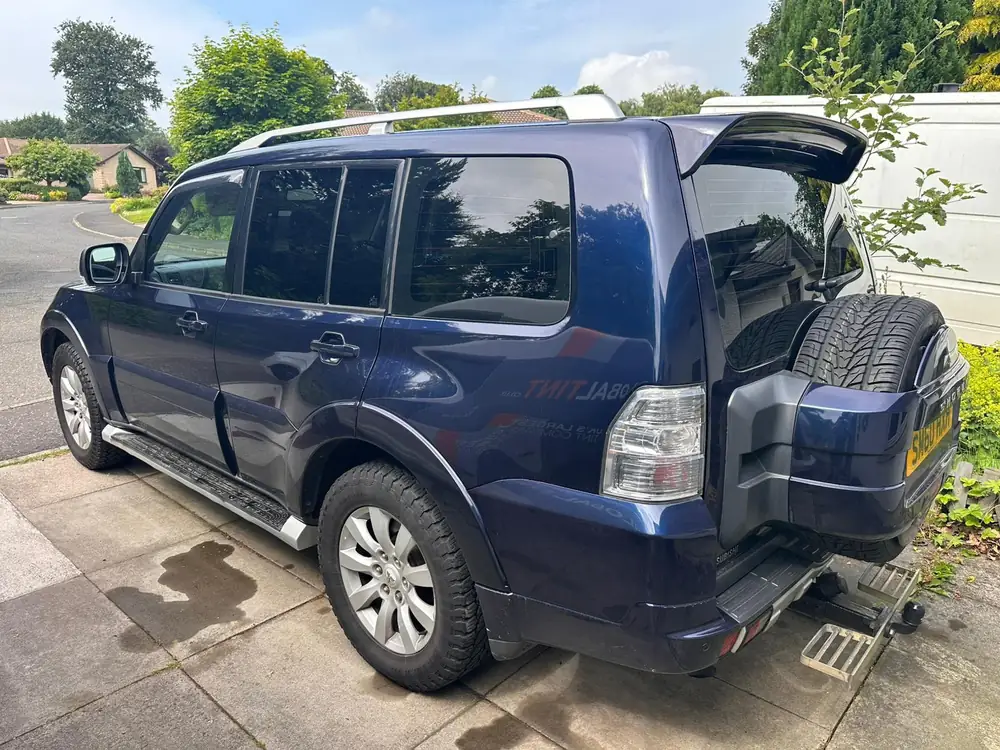 Blue Mitsubishi Shogun with dark rear windows and rear windscreen, a rear-mounted spare wheel and roof rails