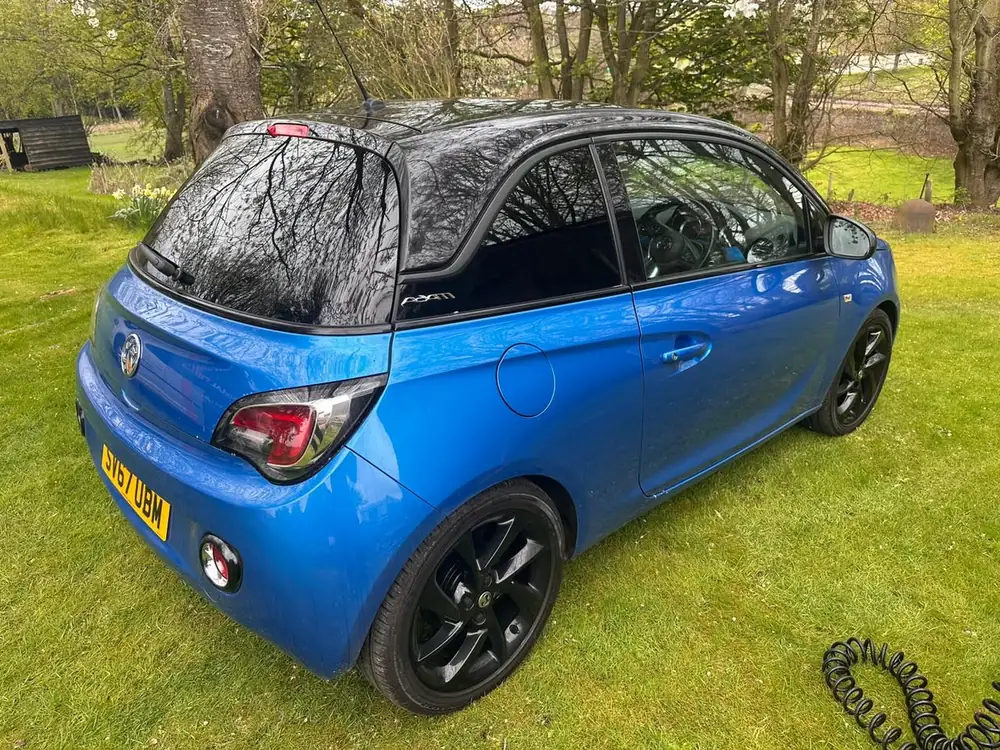 Blue Vauxhall Adam with a black roof and dark rear side glass and rear windscreen, parked on grass.