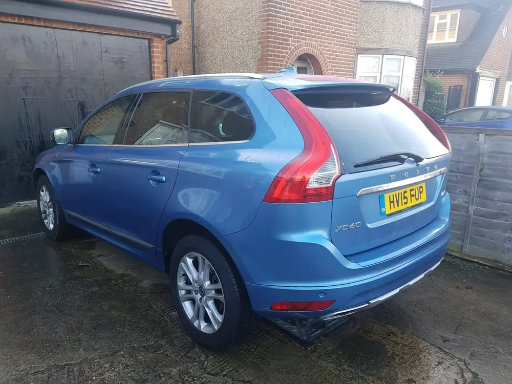 Blue Volvo XC60 parked on a driveway, viewed from the rear with reflections on the rear windows