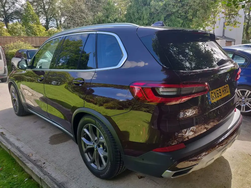 Burgundy BMW X5 with dark rear side windows and back windscreen, parked on a concrete driveway.