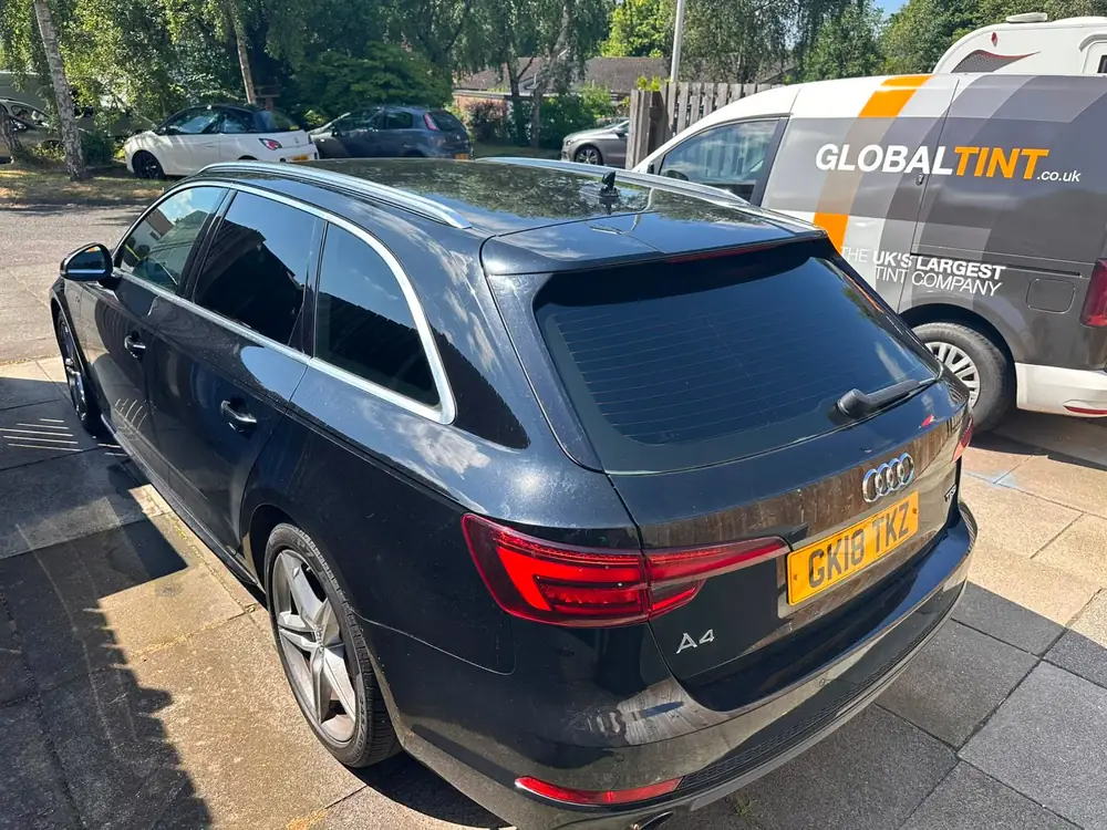 Dark blue Audi A4 Avant with dark rear side windows and back windscreen, beside a Global Tint van
