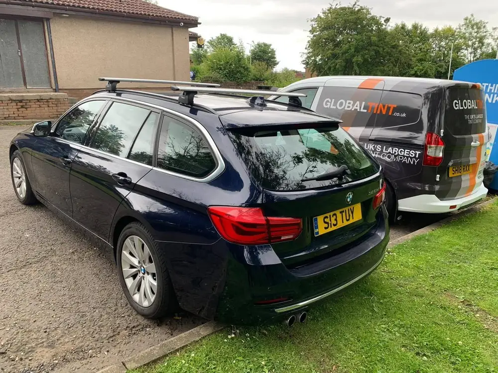 Dark blue estate with roof bars, viewed from the rear beside a Global Tint van
