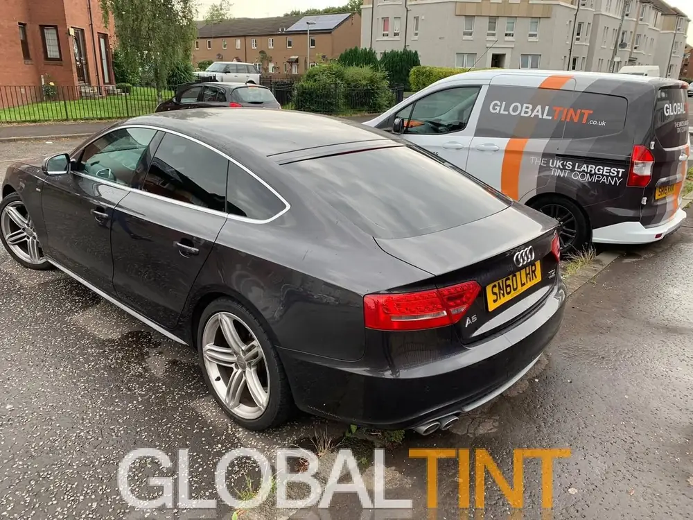 Dark grey Audi A5 with tinted rear side windows and rear windscreen, beside a Global Tint van.