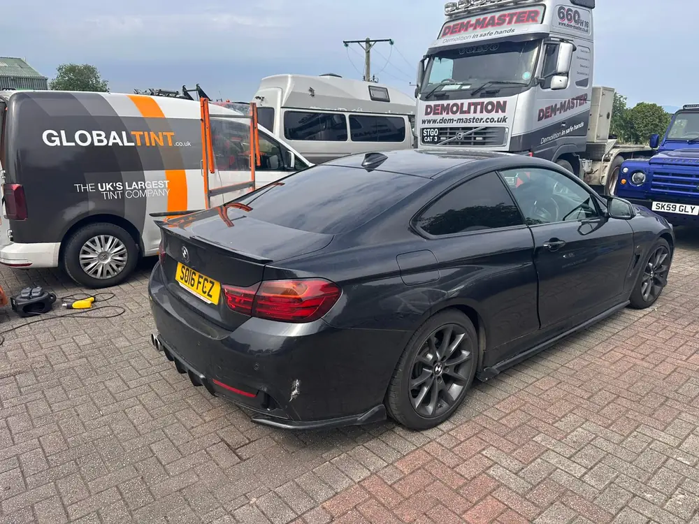 Dark grey BMW 4 Series Coupé with dark rear glass, parked beside a Global Tint van.