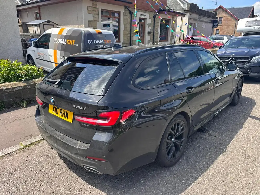 Dark grey BMW 520d Touring with dark rear side windows and rear windscreen, parked near a Global Tint van