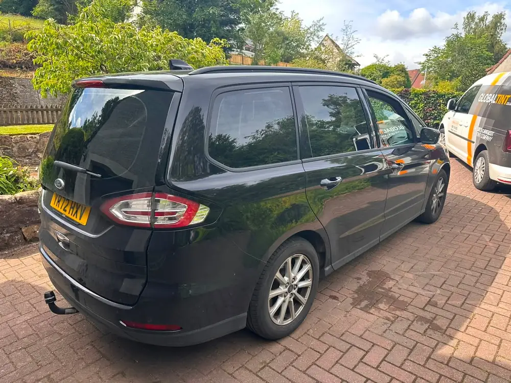 Dark grey Ford S-Max with dark rear windows, parked on a driveway beside a Global Tint van
