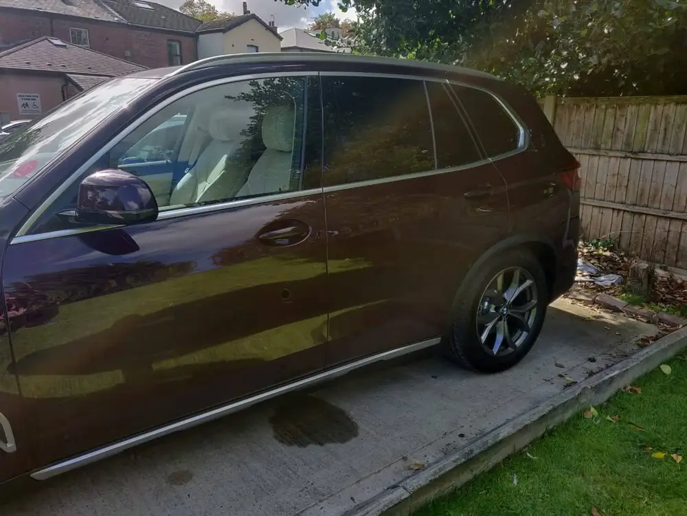 Close side view of a dark purple SUV with dark rear side windows beside a wooden fence.
