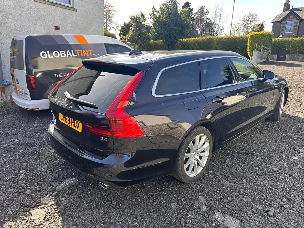 Dark-coloured Volvo V90 estate with dark rear windows and rear windscreen, parked on gravel
