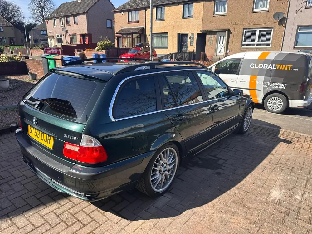 Green BMW 325i Touring with dark rear windows and rear windscreen, parked on a paved driveway