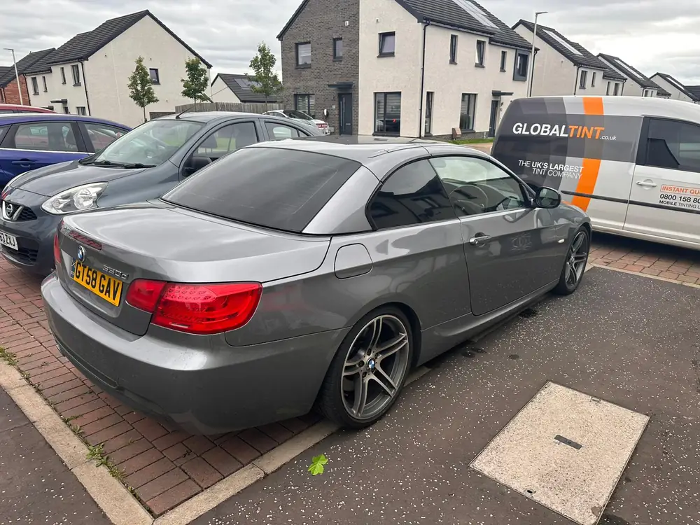 Grey BMW 3 Series Convertible with its roof up and dark rear glass, parked beside a Global Tint van