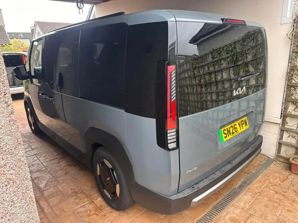 Grey Kia PV5 with dark-tinted rear side windows and rear windscreen, viewed from behind on a driveway.