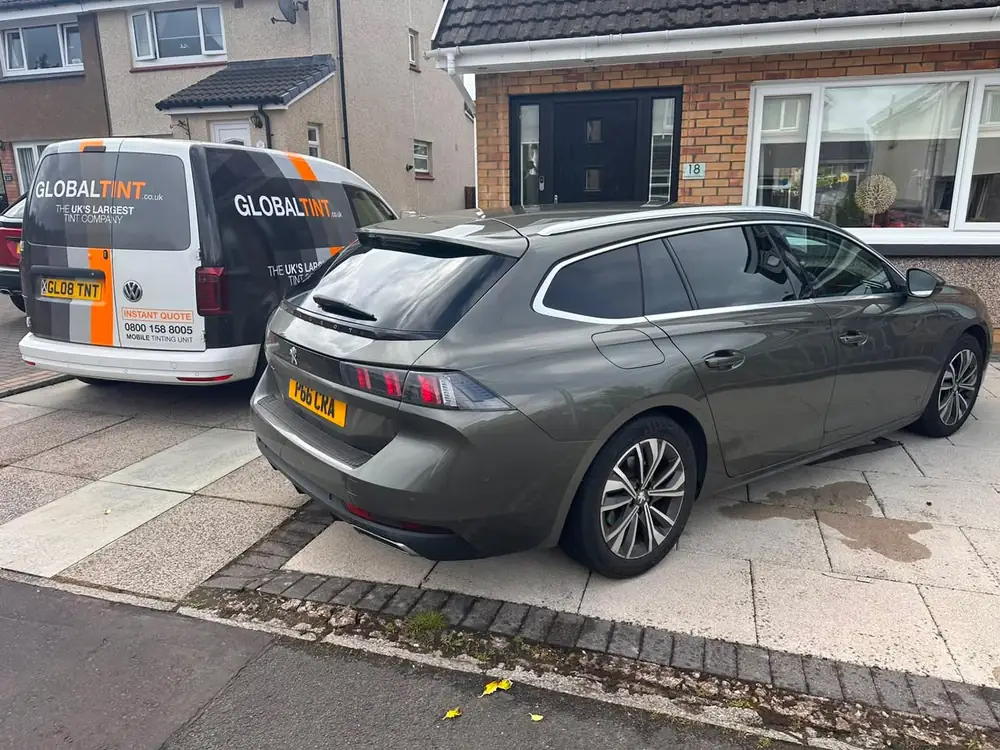 Grey Peugeot 508 SW with dark rear windows, parked on a driveway beside a Global Tint van.