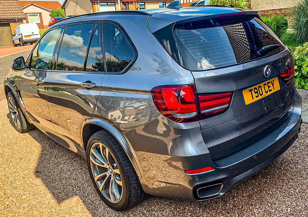 Grey SUV with dark rear side windows and rear windscreen, parked on gravel