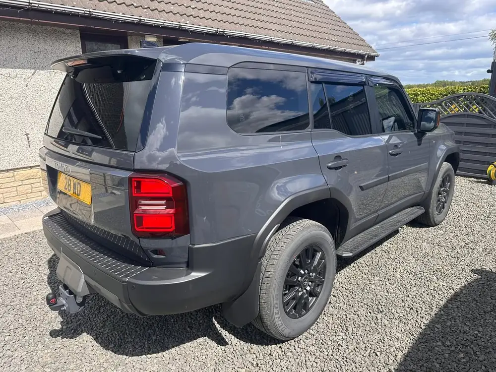 Grey Toyota Land Cruiser with dark rear side windows and rear windscreen, parked on gravel.