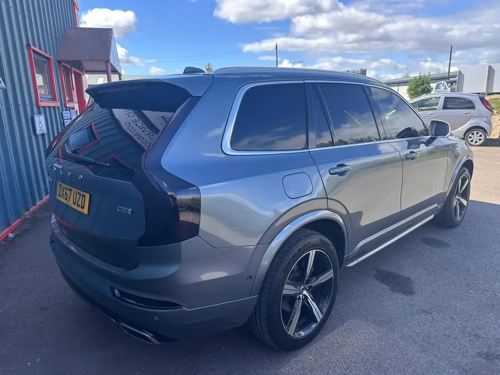 Grey Volvo XC90 with dark rear side windows and rear windscreen, parked beside a building.