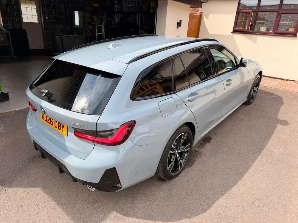 Light blue BMW 3 Series Touring with dark rear side windows and back windscreen, parked beside an open garage