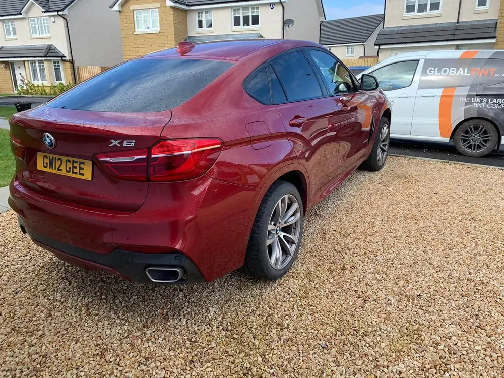 Red BMW X6 with tinted rear side windows and rear windscreen, parked on gravel beside a Global Tint van