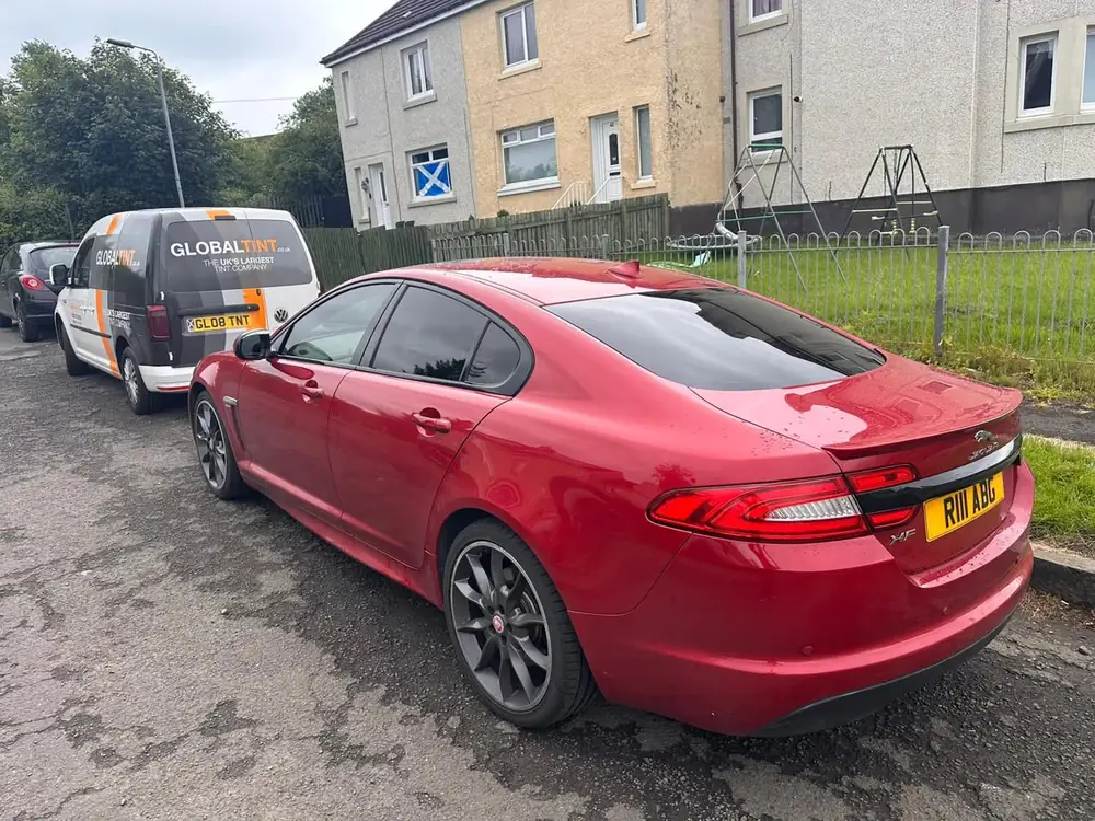 Red Jaguar XF with dark rear side windows and rear windscreen, parked beside a Global Tint van
