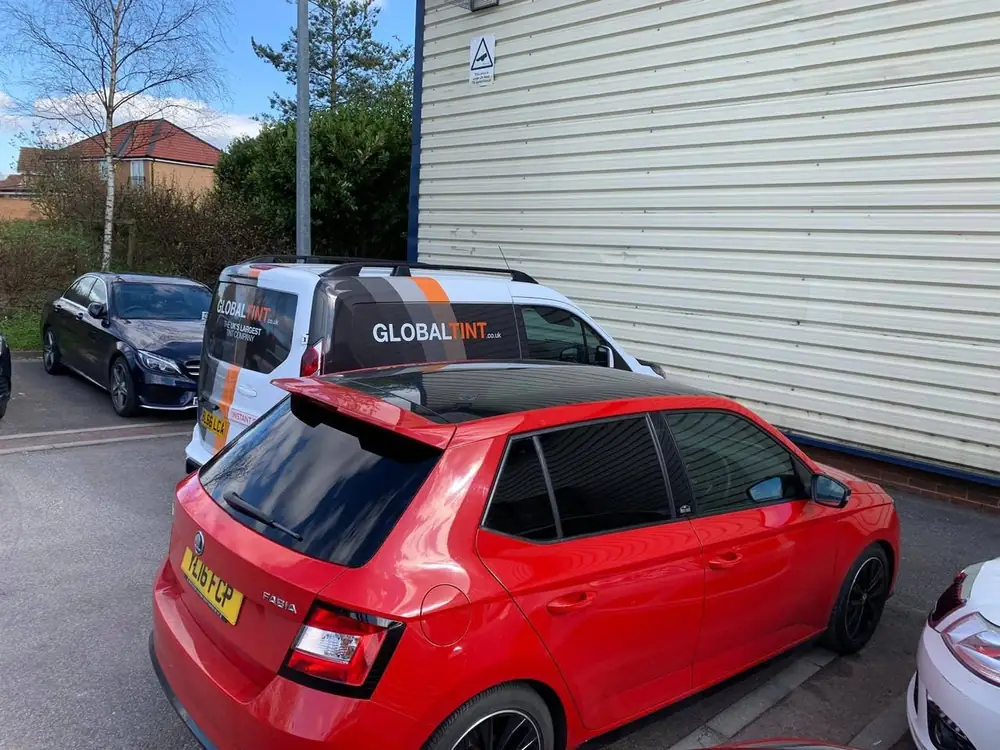 Red Skoda Fabia with a black roof, dark rear side windows and back windscreen, parked beside a Global Tint van