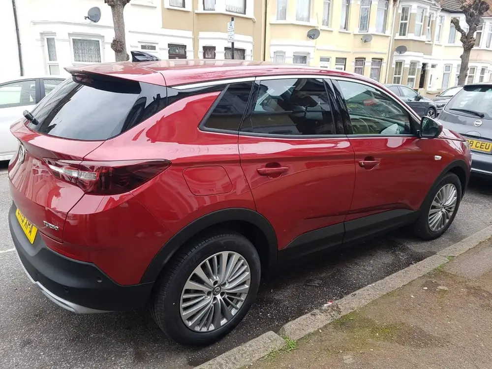 Red SUV with dark rear side windows and rear windscreen, parked beside a kerb.