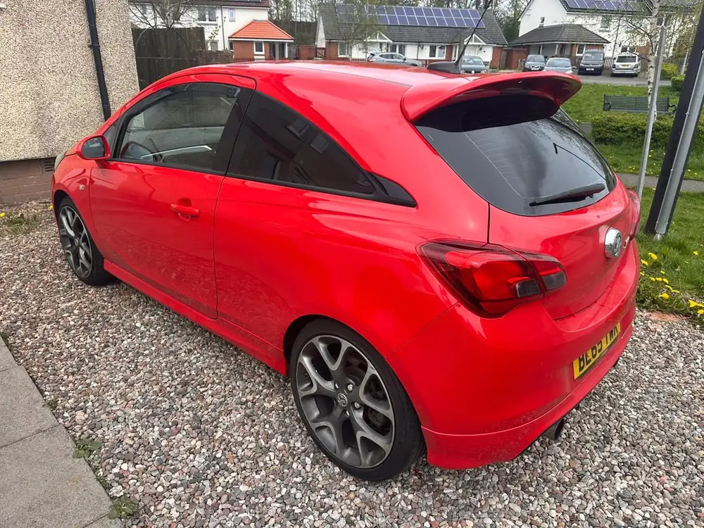 Red Vauxhall Corsa with dark rear side windows and rear windscreen, parked on gravel