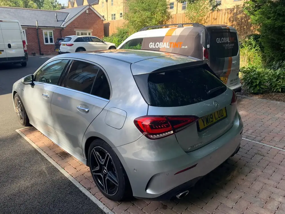 Silver hatchback with tinted rear side windows and a dark rear windscreen, parked beside a Global Tint van