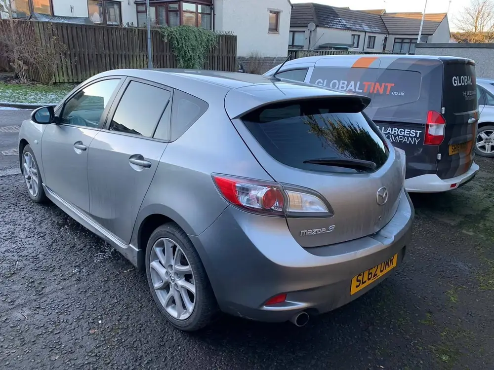 Silver Mazda 3 hatchback with dark rear windows and rear windscreen, parked beside a Global Tint van
