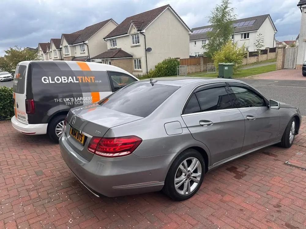 Silver Mercedes E-Class with dark rear side windows and rear windscreen, parked on a brick driveway