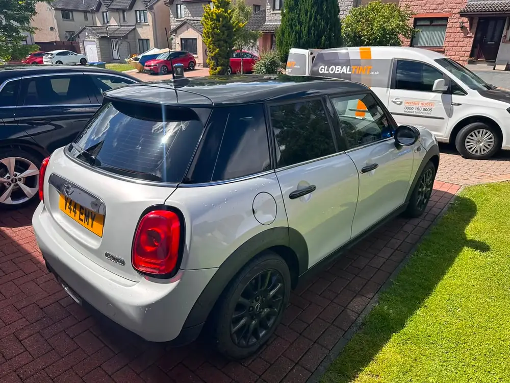Silver MINI Cooper with a black roof and dark rear side windows and rear windscreen, parked on brick paving.