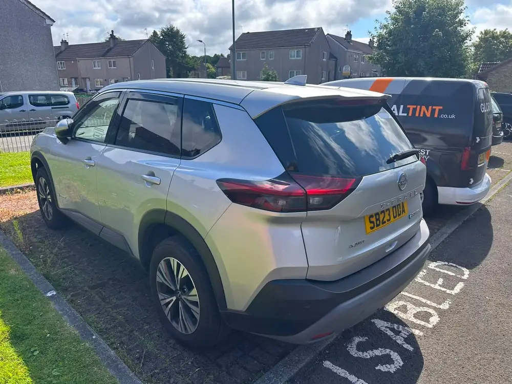 Silver Nissan X-Trail with dark rear side windows and rear windscreen, parked beside a Global Tint van.