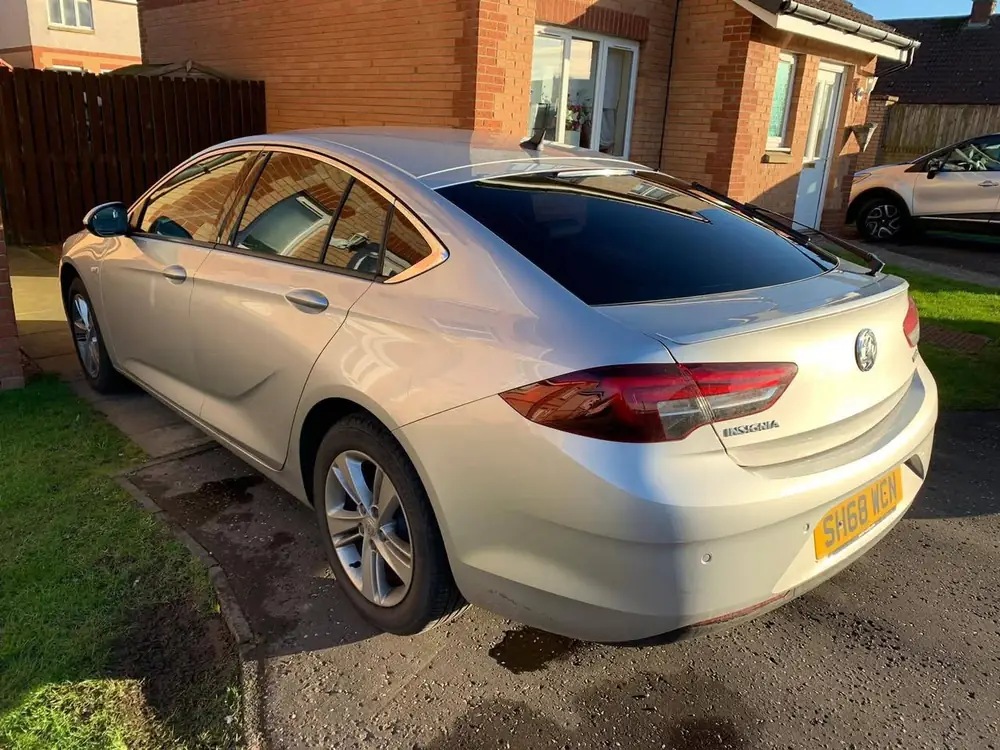 Silver Vauxhall Insignia with a dark tinted rear windscreen, parked beside a brick house.
