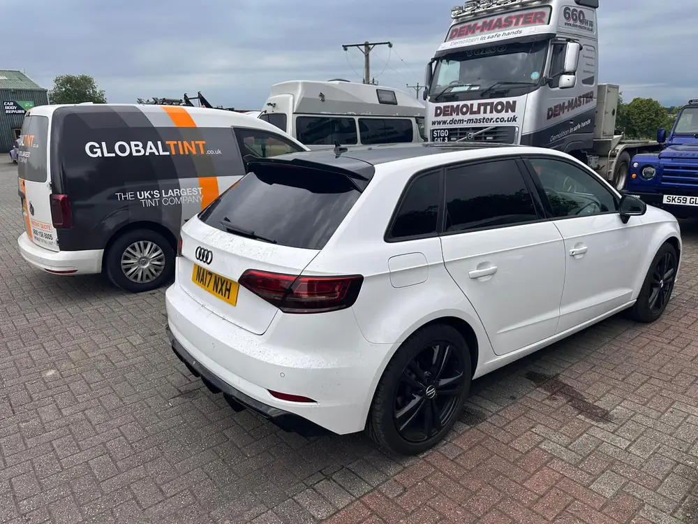 White Audi A3 with dark rear windows and black wheels, parked beside a Global Tint van