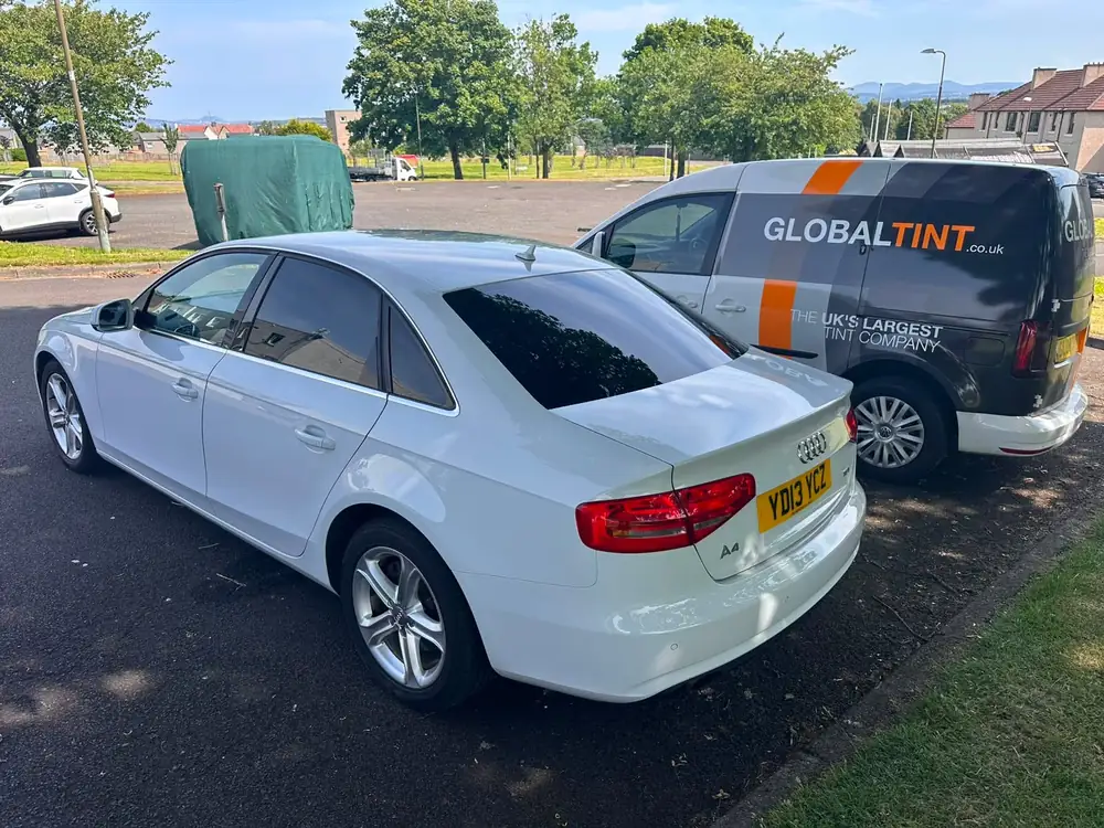 White Audi A4 with dark tinted rear side windows and rear windscreen, parked beside a Global Tint van.